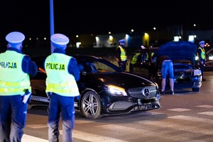 Umundurowani policjanci nocą stojący przy samochodach osobowych