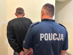 Na zdjęciu widoczny policjant z zatrzymanym stoją odwróceni plecami