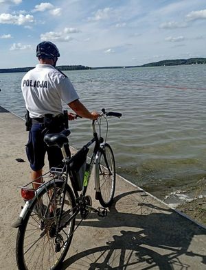 Policjant z rowerem na pomoście wpatrujący się na kompielisku