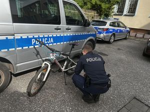 Policjant kucający przy białym rowerze, w tle stoją policyjne radiowozy