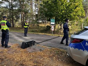 Trzech policjantów rozwijających kolczatkę na jezdni.