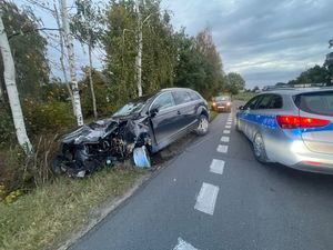 Rozbity czarny samochód typu SUV  stojący w rowie obok niego policyjny radiowóz