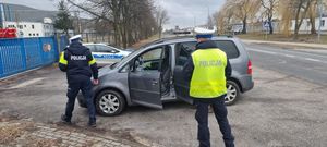 Dwóch policjantów stojących przy samochodzie z otwartymi drzwiami.