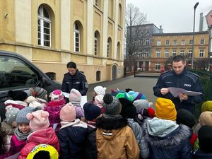 Policjantka i policjant stojący na boisku szkolnym obok nich radiowóz i grupa ludzi