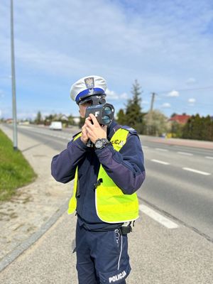 Policjant ruchu drogowego stojący przy drodze i mierżący prędkość