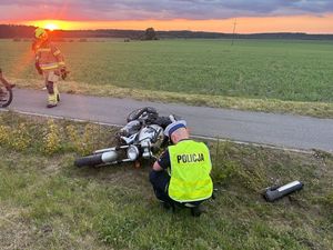 Policjant wykonujący oględziny rozbitego motocykla leżącego na poboczu drogi