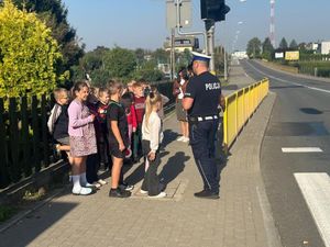 Policjant ruchu drogowego stojący przy przejściu  dla pieszych grupką dzieci.