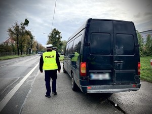 Policjant na poboczu drogi stojący przy czarnym samochodzie dostawczym.