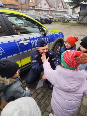 Policjant przy radiowozie przybijający ,,,piątkę&quot; jednemu z grupy dzieci