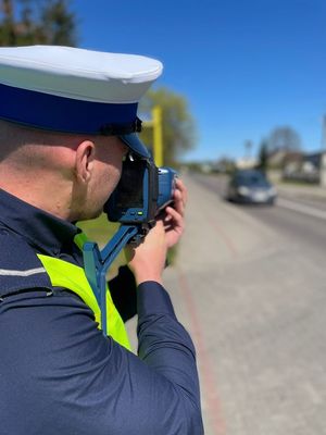 Policjant stojący przy jezdni dokonujący pomiaru prędkości nadjeżdzającego pojazdu