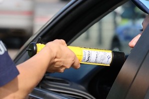 policjan prowadzacy badanie stanu trzeżwości kobiety siedzącej w samochodzie.