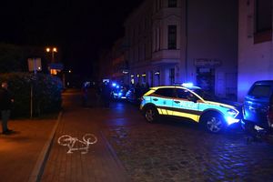 Policyjny radiowóz stojacy w nocy na ulicy, wokół niego inni ludzie.