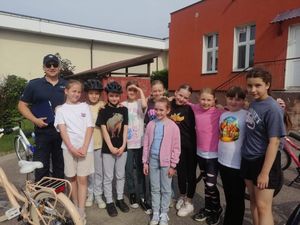 Policjant stojący razem z dziećmi przed budynkiem szkoły