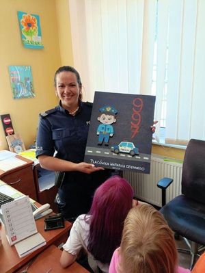 Policjantka w biurze stojąca przed grupą dzieci trzymająca w ręku tablicę