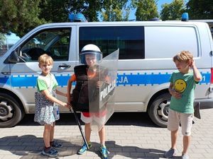 Dzieci stojące przy radiowozie z policyjną tarczą