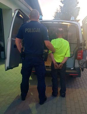 Policjanci prowadzący zatrzymanego do policyjnego radiowozu
