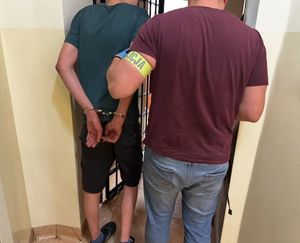 Na zdjęciu widoczny policjant kryminalny bez służbowego umundurowania z osobą zatrzymaną