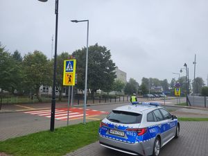 Policyjny radiowóz stojący przy szkole, widoczne przejście dla pieszych. oznakowanie pionowe i poziome