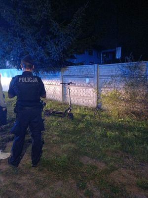 Policjant obok stojącej na trawniku hulajnogi elektrycznej