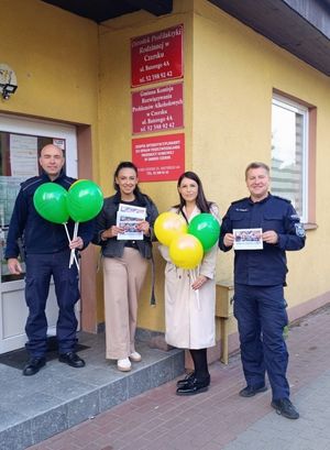 Policjanci stojący przed budynkiem z dwoma kobietami. w dłoniach trzymają ulotki i balony.