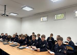 Uczniowei klasy mundurowej siedzący w szkolnych ławkach podczas zajęć z policjantką