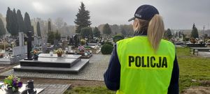 Policjantka w żółtej kamizelce odblaskowej stojąca na cmentarzu