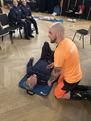 Policjant leżący na podłodze odob niego klęczy ratownik medyczny