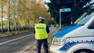 Policjant w kamizelce odblaskowej tojący obok radiowozu kytóry stoi przy ulicy