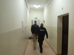 Policjant prowadzący zatzrymanego mężczyznę przez korytarz