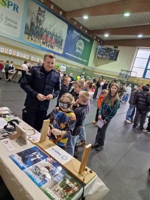 Policjant podczas Targów Czasu Wolnego Promujący zawód policjanta w hali sportowej przy stanowisku Policji