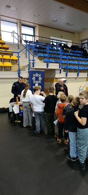 Policjant podczas Targów Czasu Wolnego Promujący zawód policjanta w hali sportowej przy stanowisku Policji