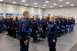 Policjant składający meldunek policjantce w sali gdzie są inni policjanci