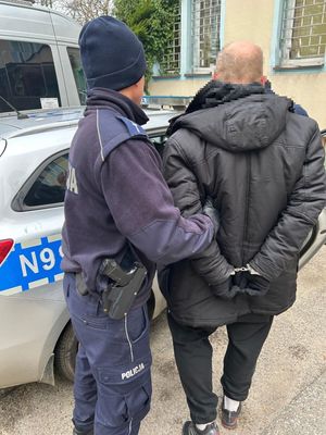 Policjant prowadzący zatzrymanego mężczyznę do raadiowozu