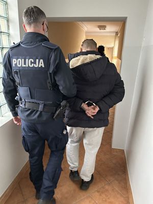Policjant prowadzący korytarzem zatrzymanego mężczyznę w kajdankach.
