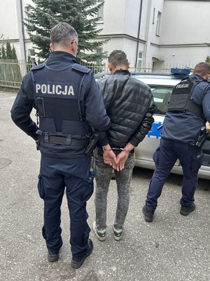 Policjanci prowadzący do radiowozu zatrzymanego męzczyznę.