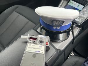 Czapka plicjanta ruchu drogowego oraz alkotest leżący na podłokietniuk wewnątrz samochodu