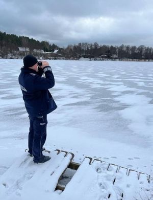 Policjant z lornetką stojący na brzegu zamarzniętego zbiorniak wodnego