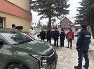 Policjanci umundurowani stoją przy radiowozie nieoznakowanym.