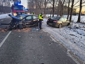 Policjanci stojący przy rozbitych samochodach stojących na drodze