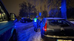 Policjant w kamizelce odblaskowej w nocnej zimowej sceneri stojący przy samochodzie obok widoczny przód radiowozu