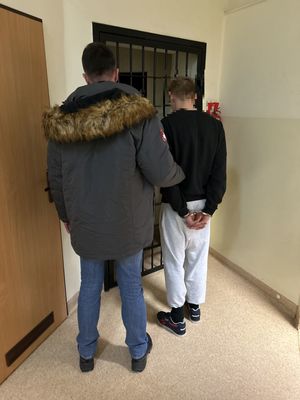 Policjant z zatrzymanym stojący przed pomieszczeniem z kratą