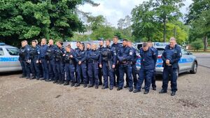 Policjani ustawieni w szeregu podczas ćwoiczeń sztabowych za nimi stoją zaparkowane policyjne radiowozy