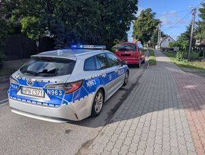 Policyjny radiowoz stojący na drodze za zatrzymanym czerwonym samochodem