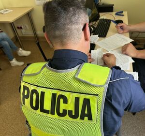 Policjant siedzący przy biurku wypełniający dokumęty.