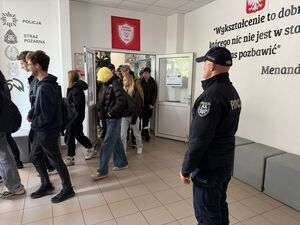 Policjant stojący w szkolnym korytarzu przy wyjściu nadzorujący wyjście z ze szkoły podczas próbnej ewakuacji
